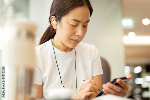 Woman working on smartphone with wireless earphones in cafe.