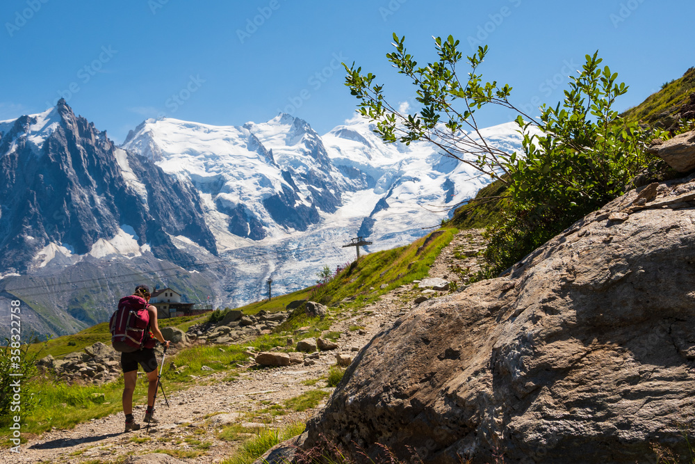 Young woman (unrecognizable, back view) hiking at Plan Praz with breathtaking view of Aiguille du Midi in Mont Blanc mountains within the French Alps in summer.