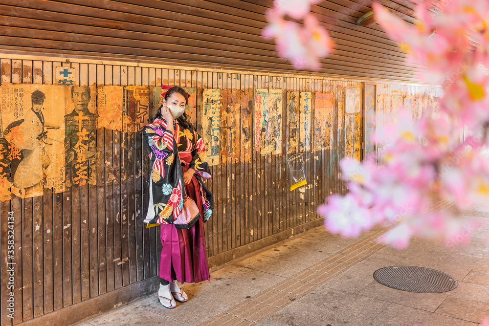 Fototapeta premium Japanese woman in hakama kimono wearing a cloth mask at retro underpass Yuraku Concourse decorated with old posters and placards glued to the walls of the tunnel who revive the nostalgic Showa era.