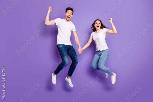 Full length photo pretty lady handsome guy couple jumping high up holding arms sporty people win race competitions wear casual t-shirts jeans pants shoes isolated purple color background