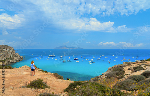 paradise clear torquoise blue water with boats and cloudy blue sky in background in Favignana island, Cala Rossa Beach, Sicily South Italy. © poludziber