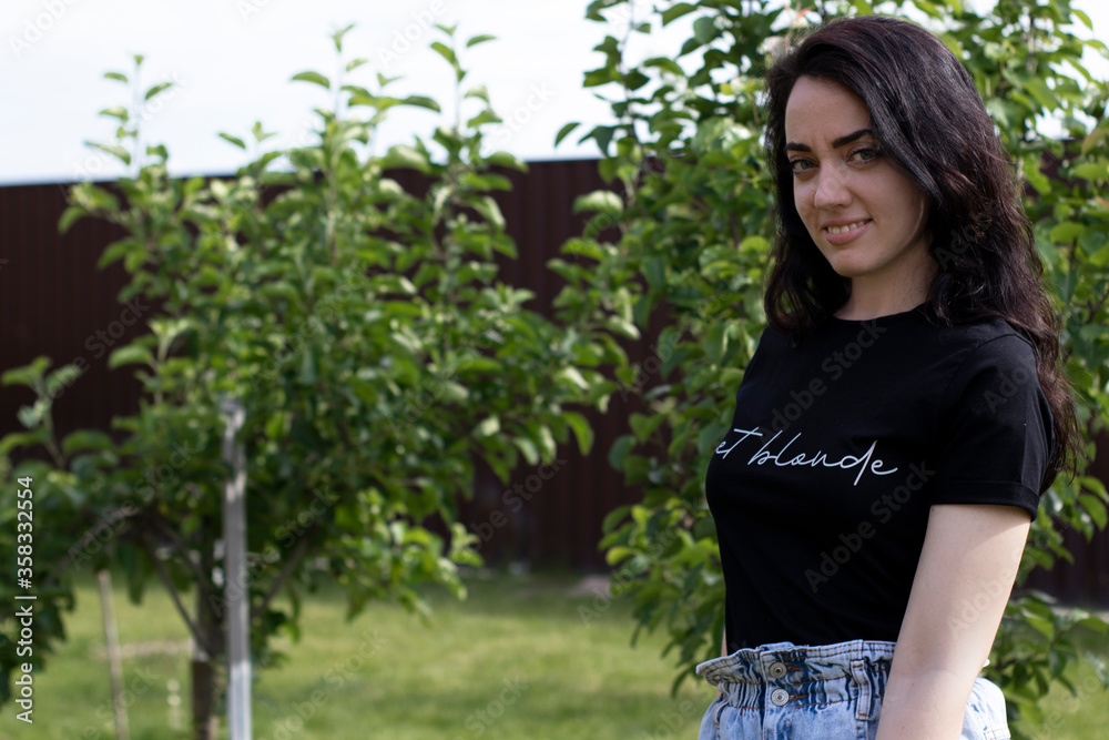 Charming young brunette woman in a black T-shirt and denim shorts. In the country, in the garden. High quality photo Charming young brunette woman in a black T-shirt and denim shorts. In the country, in the garden. High quality photo