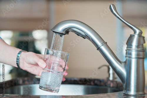 close up of a hand filling up a glass of water from a sink