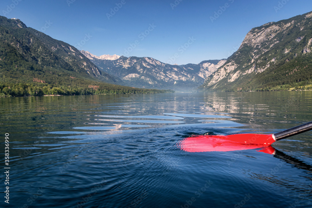 Pristine mountain lake Bohinj in Slovenia. View from kayak with red paddle. Dark blue water and amazing landscape with Alps mountains in background. Early morning paddling