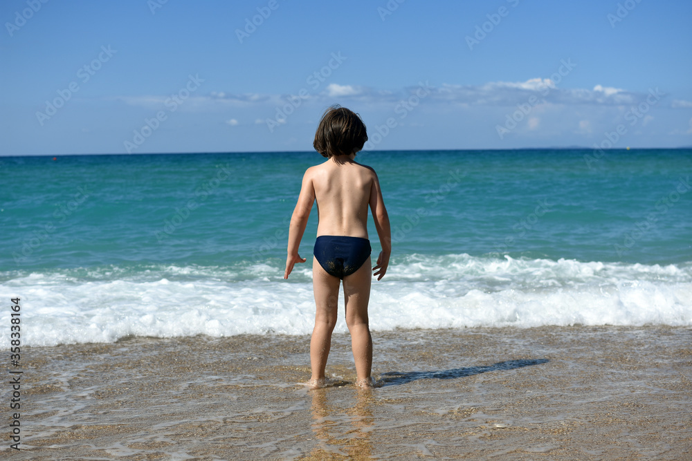 Little boy enjoying on beach. Child sit on beach and play in sea on summer vacation Little boy enjoying on beach. Child sit on beach and play in sea on summer vacation