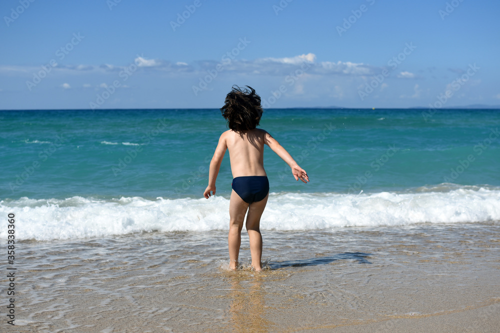 Little boy enjoying on beach. Child sit on beach and play in sea on summer vacation