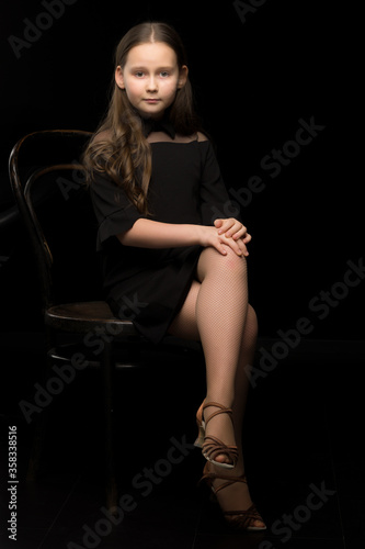 Portrait of a little girl sitting on an old Viennese chair, black background.