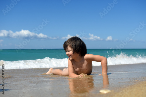 Little boy enjoying on beach. Child sit on beach and play in sea on summer vacation