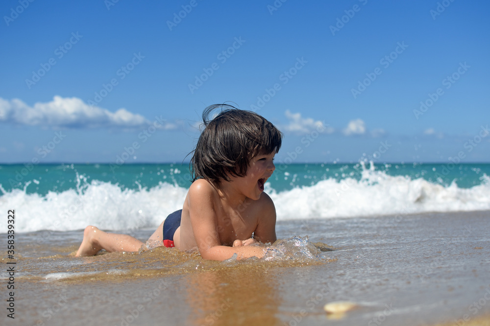 Little boy enjoying on beach. Child sit on beach and play in sea on summer vacation Little boy enjoying on beach. Child sit on beach and play in sea on summer vacation