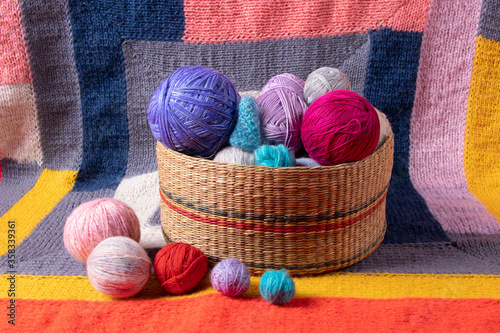 balls of multi-colored yarn in a wicker basket on the background of a multi-colored knitted bedspread