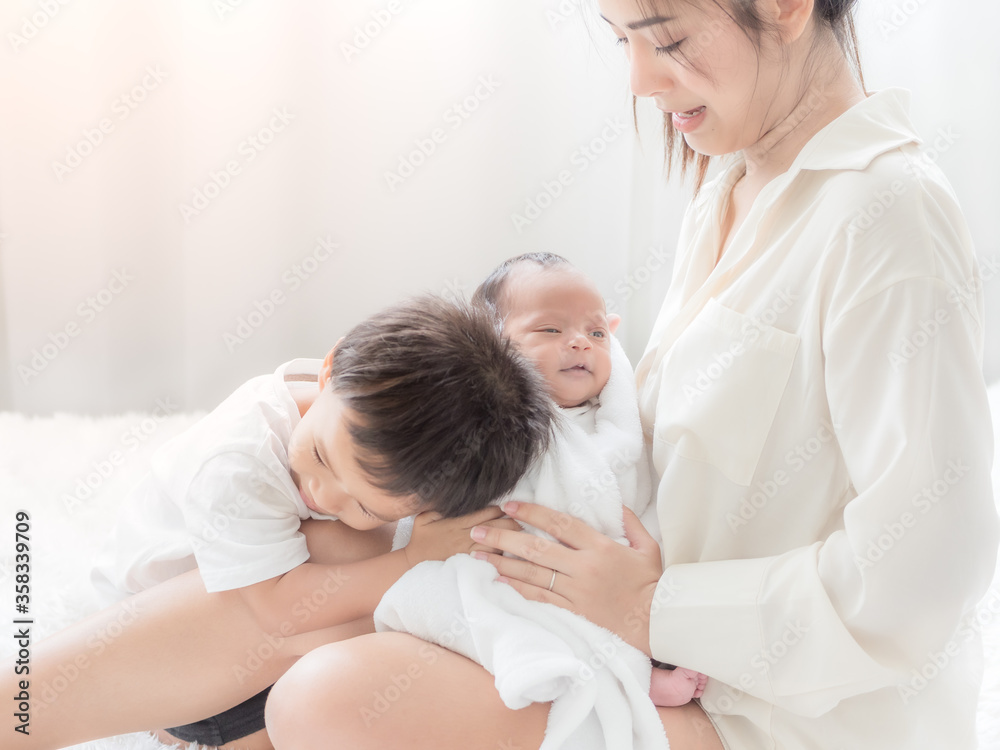 A beautiful Asian woman holds her newborn daughter and her son hugs his sister with love as well A beautiful Asian woman holds her newborn daughter and her son hugs his sister with love as well