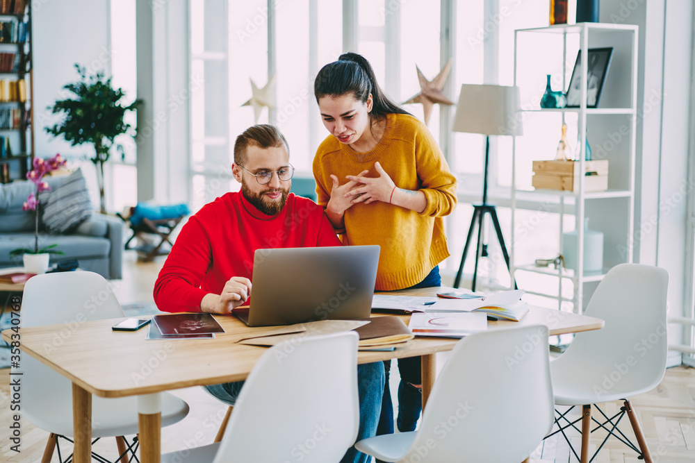 Young woman talking with male colleague consulting about updating app on netbook for online working, partners having conversation watching video on laptop computer cooperating in coworking space