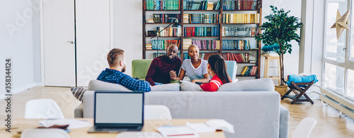 Couples having meeting in hostel communicating in modern designer room with bookshelves, young marriage happy to having conversation with guests friends resting on laisure in apartment together photo