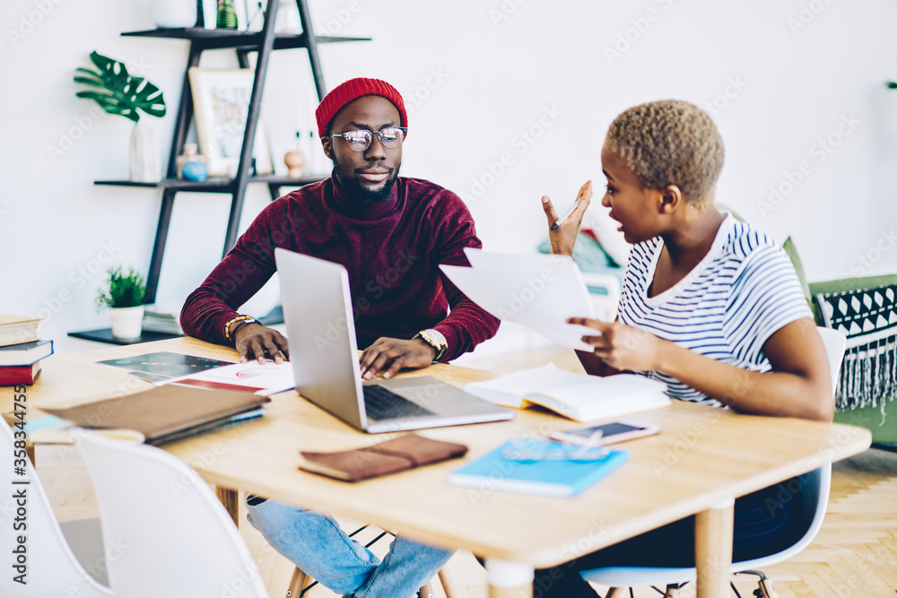 Serious dark skinned male and female colleagues having discussion during working process disappointed with planning, angry african american woman quarrel with hipster guy checking documents Serious dark skinned male and female colleagues having discussion during working process disappointed with planning, angry african american woman quarrel with hipster guy checking documents