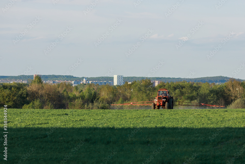 Obraz premium Tractor spraying pesticides on field with sprayer at spring