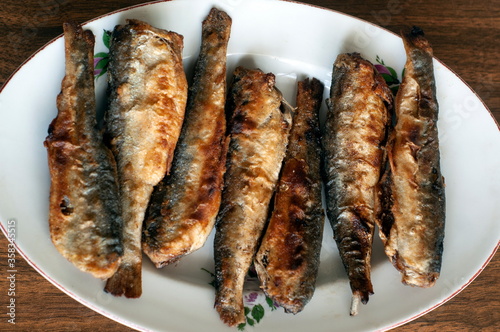 Fried fish in a white plate on a wooden table