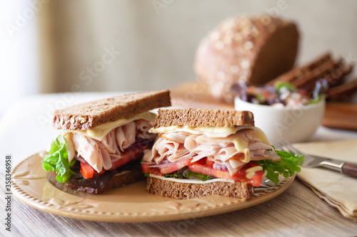 Sandwich for lunch stacked turkey or chicken sliced tomatoes cheese and lettuce red onion with mayo on fresh baked homemade bread in natural light with a small side salad