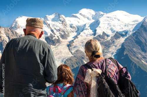 Family holidays in mountains. Senior man and woman with their granddaughter admiring snow cover Mont Blanc mountain in Alps. Back view. Elderly wellness, family together, healthy lifestyle concepts.