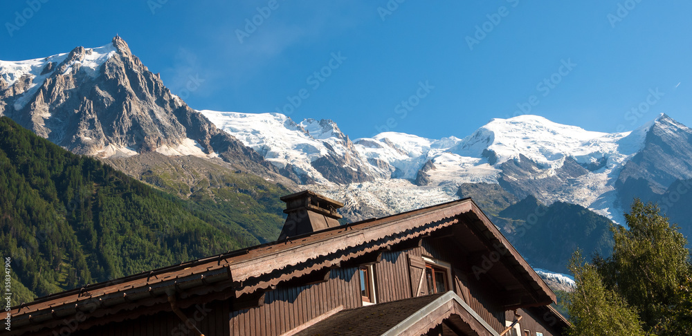 French Alps summer vacation background. Beautiful Alpine landscape with snow covered Mont Blanc mountain in and traditional wooden chalet house. Chamonix, France. Haute-Savoie tourism concept.