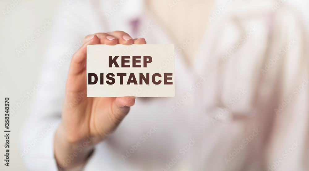 Doctor holding a card with the word KEEP DISTANCE text, medical concept. A call for people to keep their distance from each other. COVID-19 Coronavirus Doctor holding a card with the word KEEP DISTANCE text, medical concept. A call for people to keep their distance from each other. COVID-19 Coronavirus