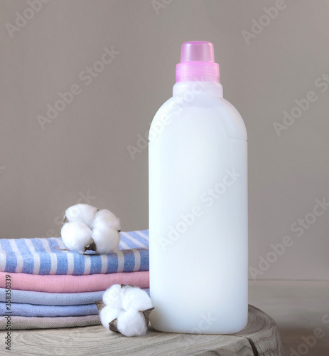 One bottle of white fabric softener and stack of towels with cotton flowers on a wooden table. Laundry day. Mockup