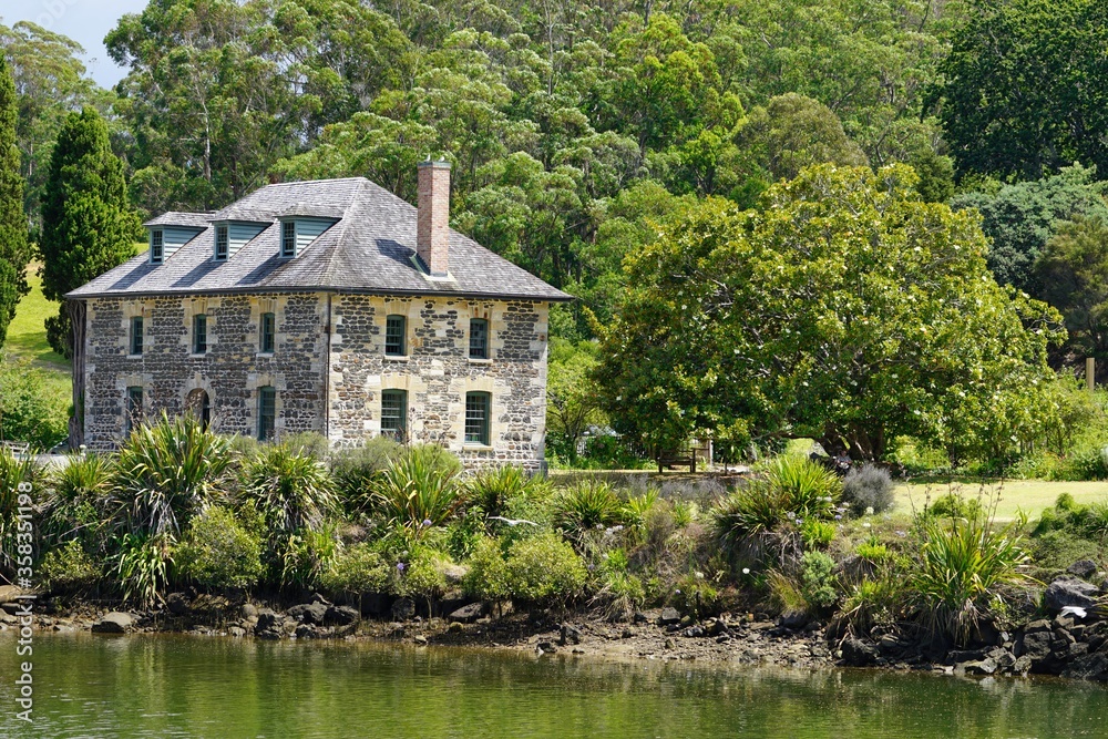 Historical Mission Station - Stone Store house in Kerikeri surrounded by green trees and plants. Lake and shore on front.