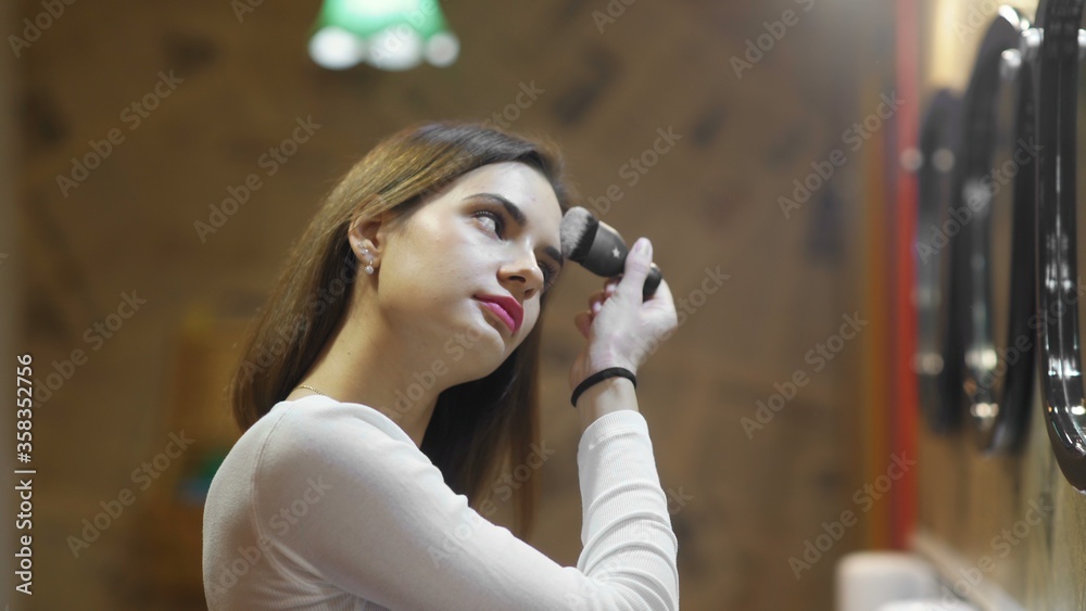 Young beauty woman uses big brush with powder in hotel public toilet