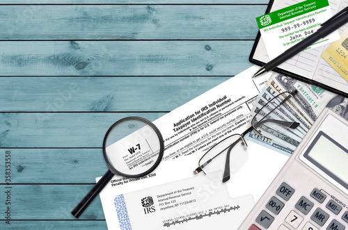 IRS form W-7 Application for IRS individual taxpayer identification number lies on flat lay office table and ready to fill. U.S. Internal revenue services paperwork concept photo