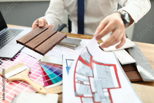 Close-up of professional worker busy with new building project. Creative architect in stylish costume sitting in cabinet. Colourful palette with samples. Renovation and interior design concept