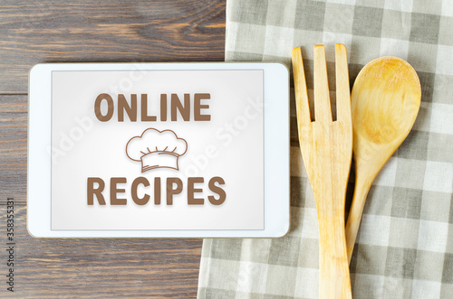 Online recipes. Cookbook in a tablet computer. Kitchen utensils. Brown wooden background
