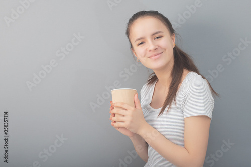 Fragrant, warming coffee in a glass. Young woman drinks hot drink on gray background