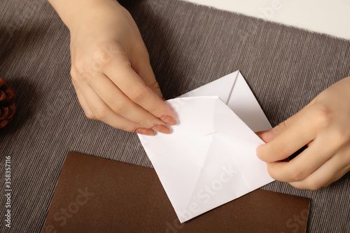 Origami is an ancient Chinese art of folding paper. Young woman makes a stick figure on a cozy brown background with lights and a warm lamp