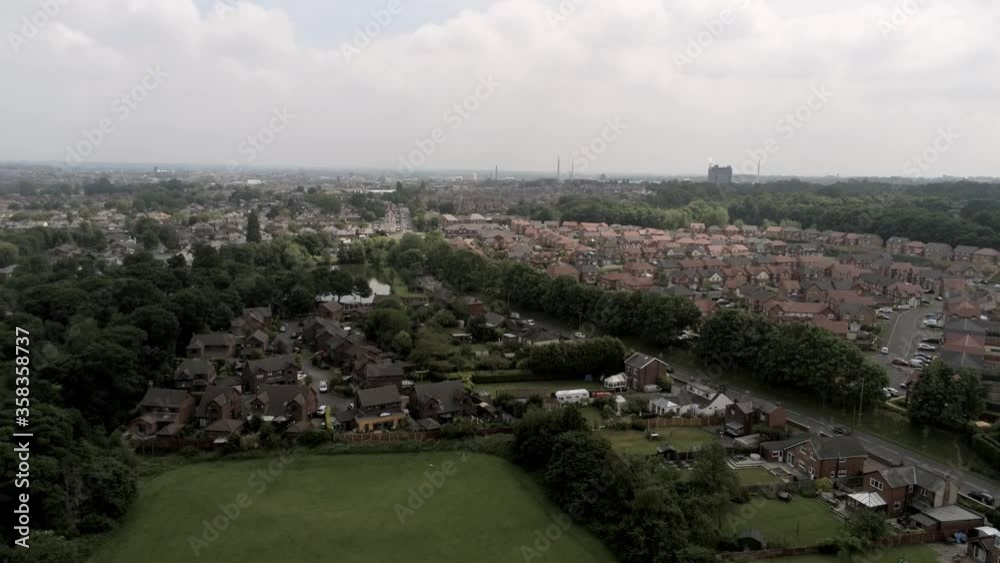 Aerial view above British Northwest neighbourhood housing estate rooftops ascending tilt down