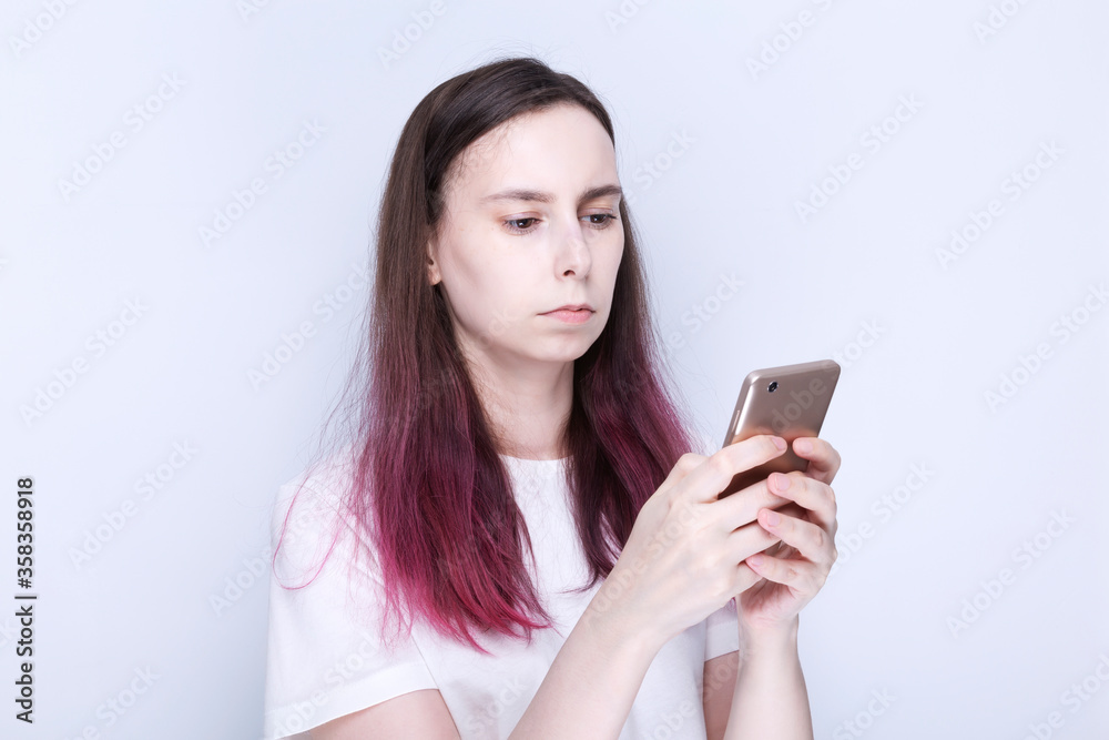 Young woman looks thoughtfully at phone, gray background Young woman looks thoughtfully at phone, gray background