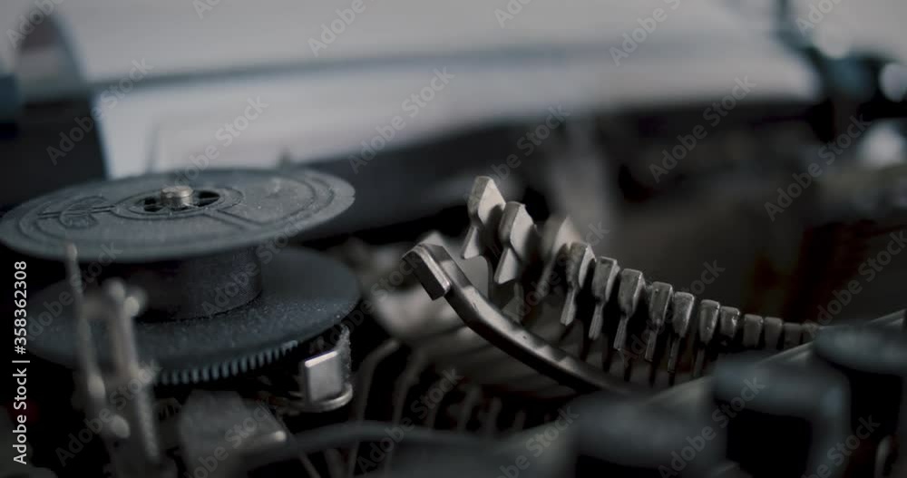 Close-up ribbon of an old vintage typewriter with metal bolts writing text in background - Slow Motion