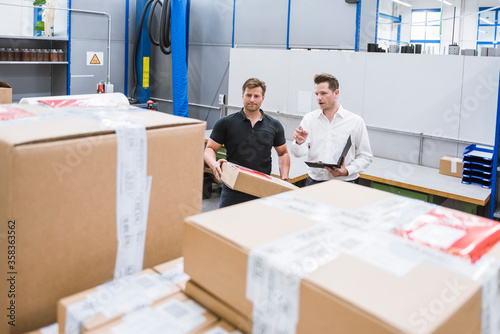Two men with parcel and clipboard in storehouse of a factory