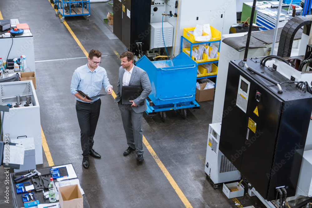 Two businessmen with clipboard talking in factory