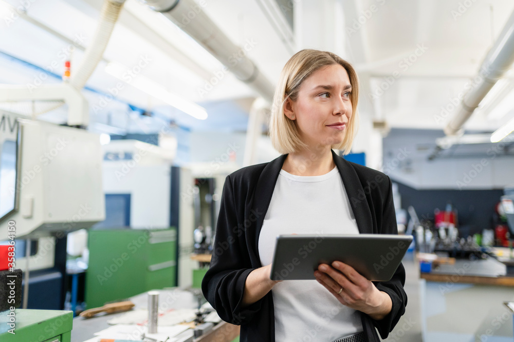 Woman holding tablet in factory hall looking around