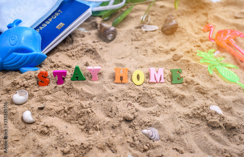 Beach sand, shells, summer, and words in wood letters stay at home.
