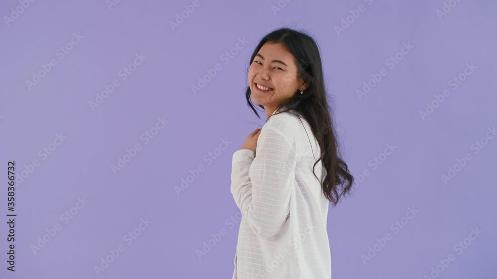 Asian lady in white shirt. She using cellphone, smiling, making a wish crossing her fingers, saying yes. Posing on purple background. Close up Asian lady in white shirt. She using cellphone, smiling, making a wish crossing her fingers, saying yes. Posing on purple background. Close up