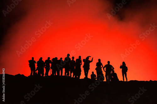 Group of unrecognized silhouettes of people standing on the edge of Erta Ale Volcano  illuminated with red lava smoke  Danakil Depression  Ethiopia  Adventure travel in Africa
