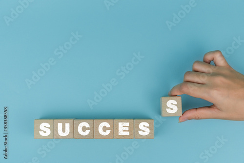 Female hand placing wood blocks on table with success text concept