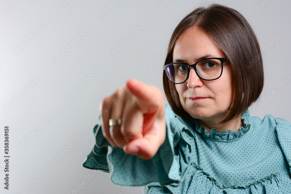 Beautiful young business woman in shirt is looking and pointing at camera, on gray background. Portrait Of A Happy Young Woman Pointing At You against a grey background. Beautiful young business woman in shirt is looking and pointing at camera, on gray background. Portrait Of A Happy Young Woman Pointing At You against a grey background.