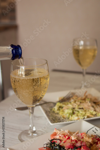 Beautiful glass transparent glasses with champagne and white square plates with food stand on a light wooden table
