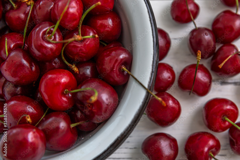 Scattered berries of ripe cherries on a light wooden background and in a bowl. Top view. Seasonal Vitamins. Scattered berries of ripe cherries on a light wooden background and in a bowl. Top view. Seasonal Vitamins.