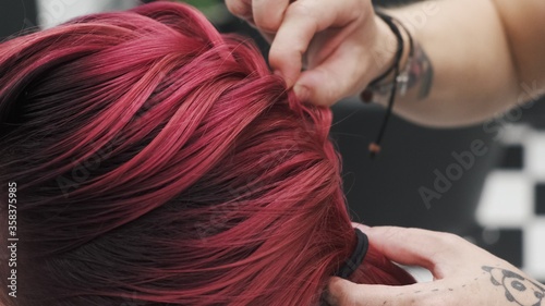 Professional hairdresser plaiting braids to red colored female hair