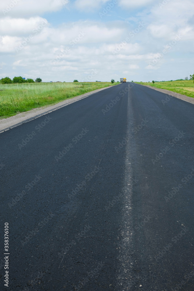 New black asphalt. There is no road marking. Reconstruction of the road in Ukraine on a hot day. Copy space. Vertical image.
