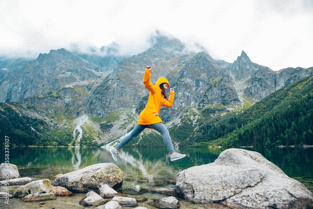 woman jumping from rock at beach lake in mountains