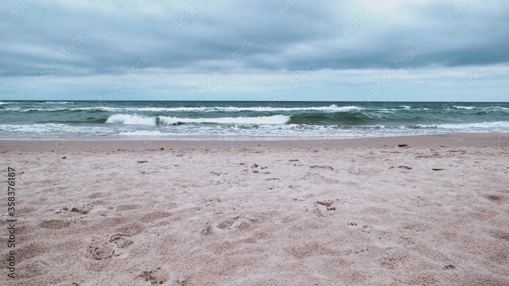 Obraz premium Cloudy rainy day at Baltic Sea. Beautiful sand beach with soft wave in sea water
