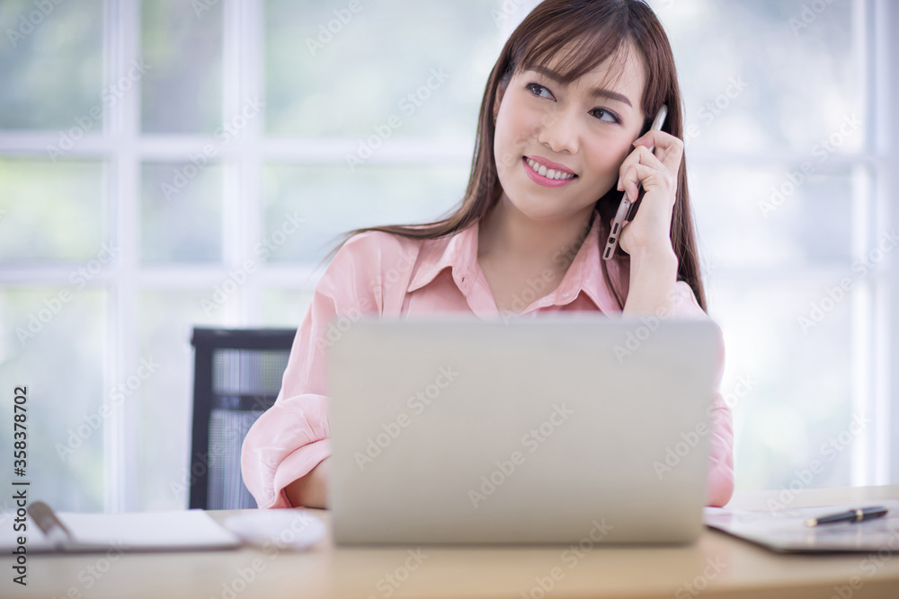 Beautiful Asian woman is talking on the phone in the office. and typing on keyboard. Asian business people, employee concept Beautiful Asian woman is talking on the phone in the office. and typing on keyboard. Asian business people, employee concept